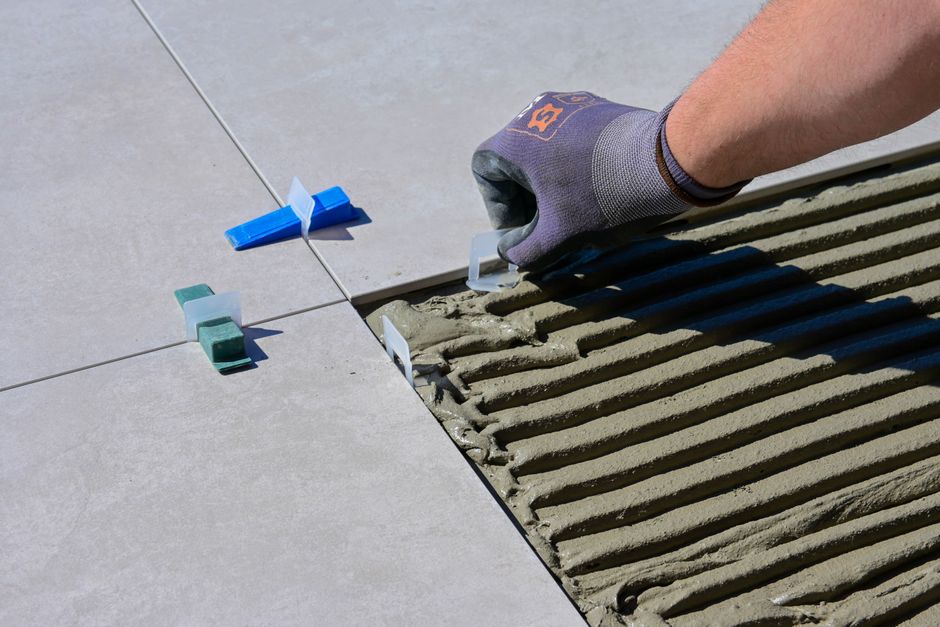 Artisan posant du carrelage au sol lors d'une rénovation de salle de bain, poste de dépense important du budget